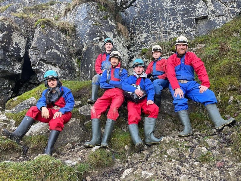 Group of young people dressed in outdoor gear sitting on a rock.