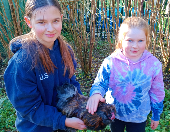 Two young people, one holding a chicken and the other stroking it.