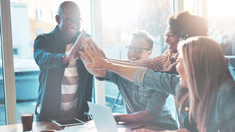 Four people sat around a computer putting their hands together.